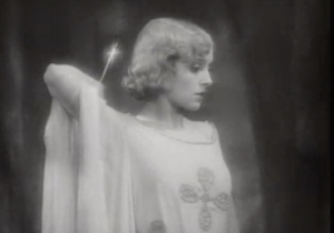 With short, wavy blonde hair, Madeleine (Madge Bellamy) holds a gleaming knife behind her head as she stares down blankly.