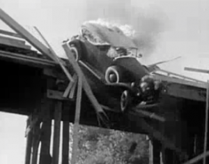 A flaming car crashes through a guardrail off a high bridge.