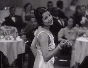 In a silky white dress, Ethel (Lena Horne) looks over her shoulder as she sings on the empty dance floor of a posh nightclub, watched by elegantly dressed Black patrons.